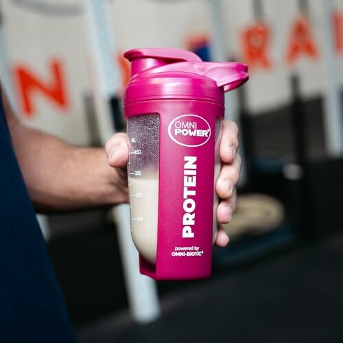 Person hält rosa Protein-Shaker im Fitnessstudio.